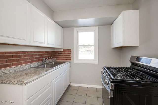 kitchen featuring stainless steel range with gas cooktop, sink, light tile patterned floors, and white cabinets