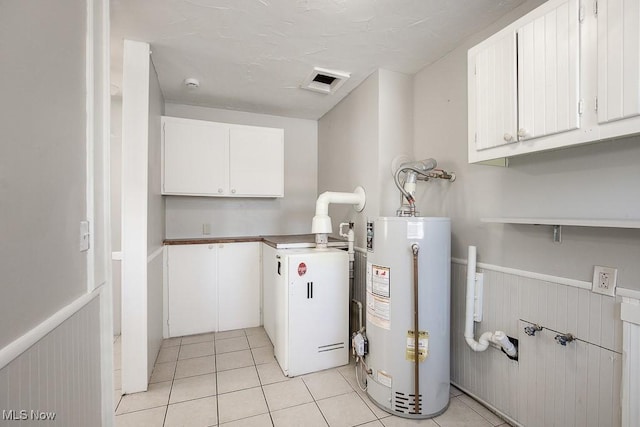 washroom with cabinets, gas water heater, light tile patterned floors, and wooden walls