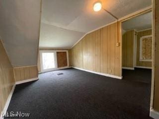 bonus room with lofted ceiling, dark carpet, and wooden walls