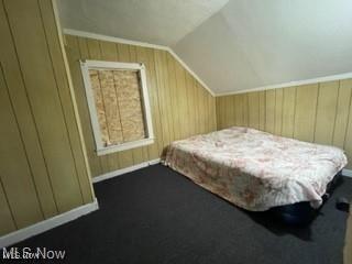 bedroom featuring lofted ceiling, dark carpet, and wood walls