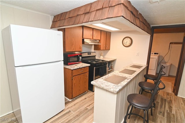 kitchen with gas range, a kitchen breakfast bar, a textured ceiling, and white refrigerator