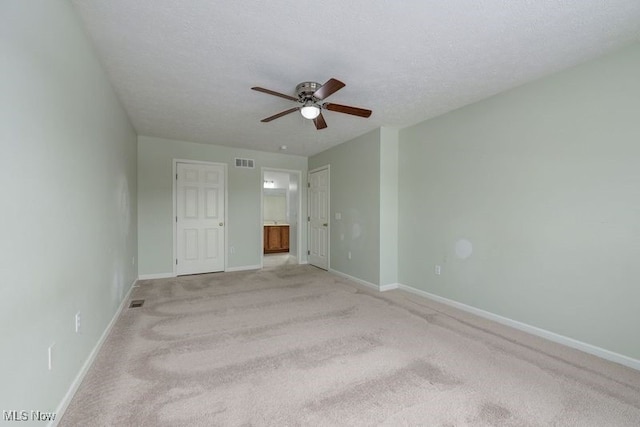 unfurnished bedroom featuring ensuite bath, ceiling fan, light carpet, a textured ceiling, and a closet