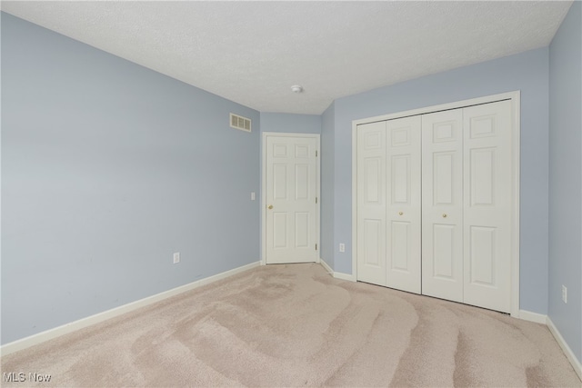 unfurnished bedroom with light carpet, a closet, and a textured ceiling