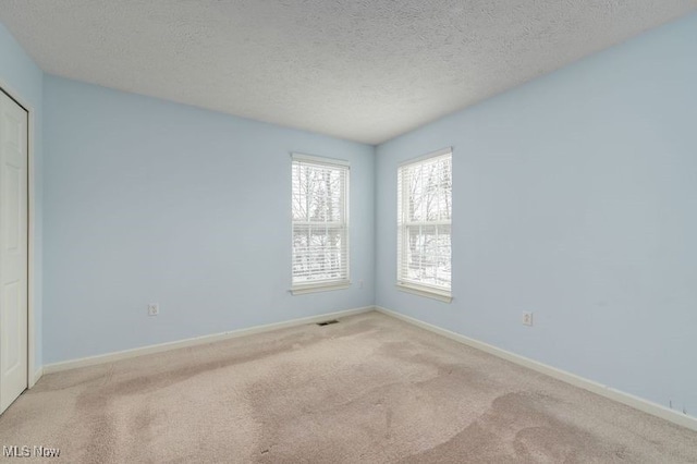 empty room with light colored carpet and a textured ceiling