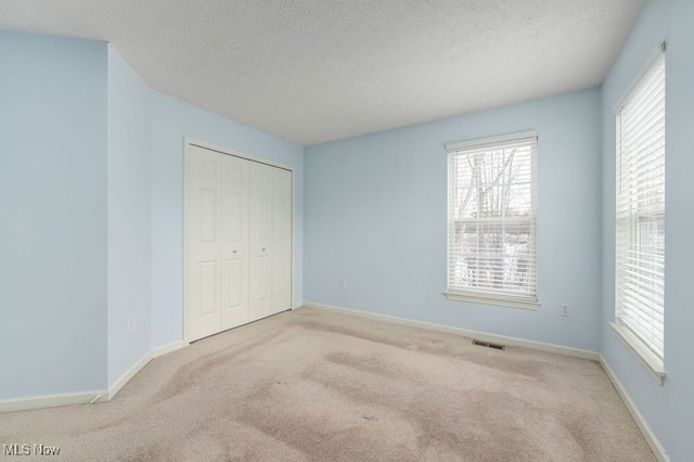 unfurnished bedroom featuring light colored carpet, a closet, and a textured ceiling