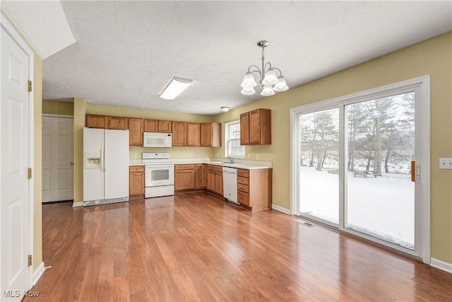 kitchen featuring decorative light fixtures, a textured ceiling, a notable chandelier, hardwood / wood-style flooring, and white appliances