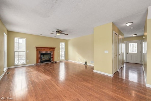 unfurnished living room featuring a brick fireplace, wood-type flooring, a textured ceiling, and plenty of natural light