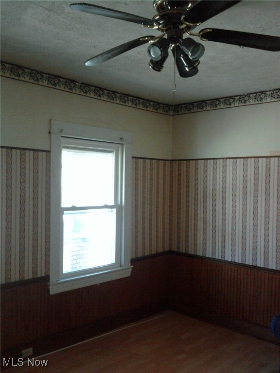 unfurnished room with ceiling fan, wood-type flooring, wooden walls, and a textured ceiling