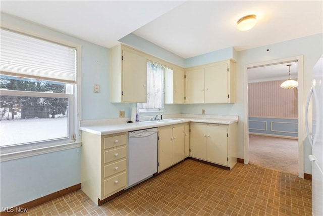 kitchen with sink, white appliances, hanging light fixtures, cream cabinets, and a chandelier