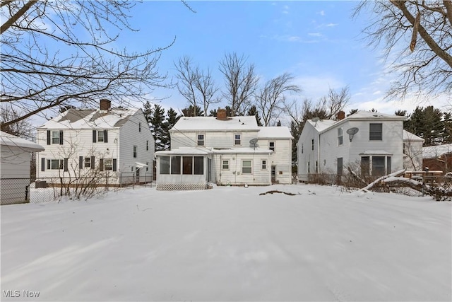 snow covered rear of property with a sunroom