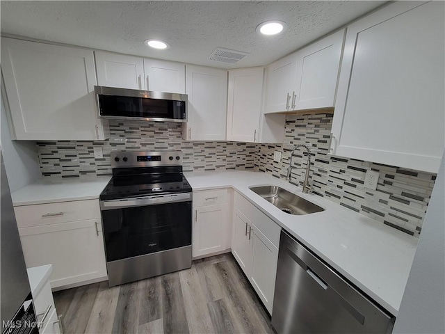 kitchen with sink, white cabinetry, stainless steel appliances, light hardwood / wood-style floors, and backsplash