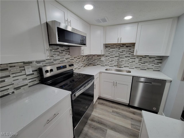 kitchen with sink, light hardwood / wood-style flooring, appliances with stainless steel finishes, backsplash, and white cabinets