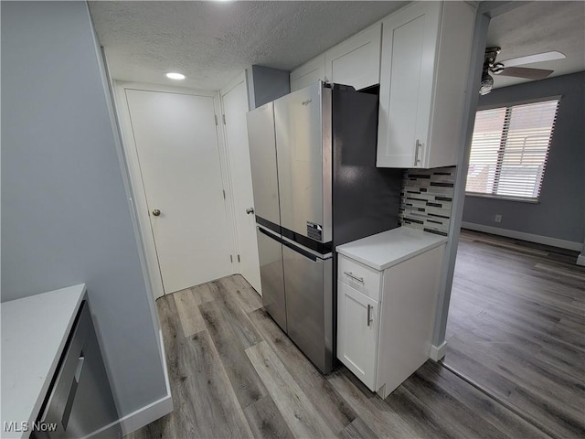 kitchen with stainless steel fridge, light hardwood / wood-style floors, white cabinets, a textured ceiling, and decorative backsplash