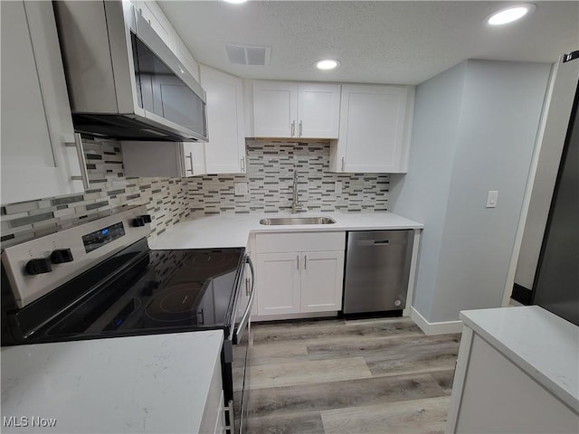 kitchen featuring white cabinetry, sink, decorative backsplash, stainless steel appliances, and light hardwood / wood-style flooring