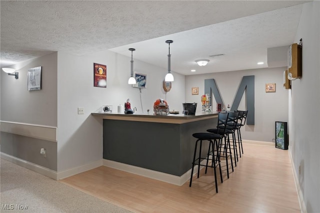 bar featuring decorative light fixtures, a textured ceiling, and light wood-type flooring