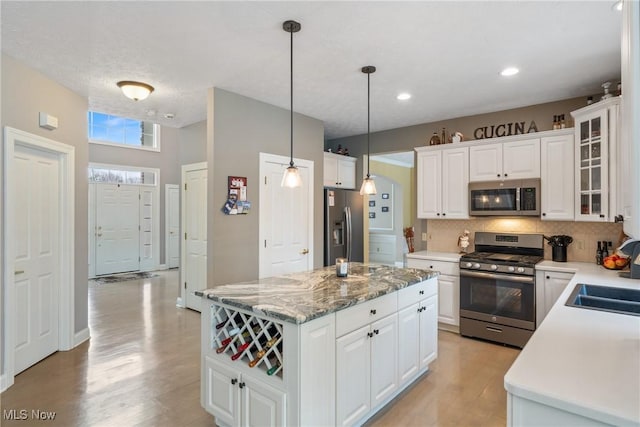 kitchen featuring a kitchen island, decorative light fixtures, tasteful backsplash, white cabinetry, and stainless steel appliances