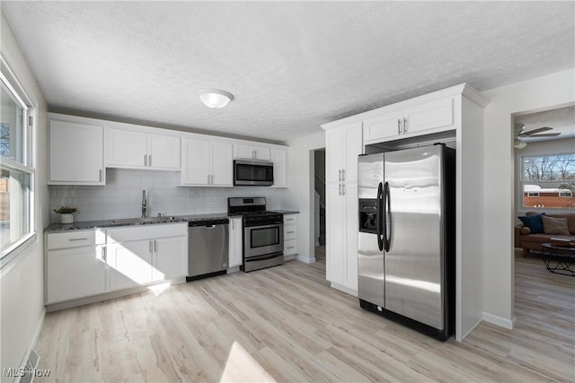 kitchen with sink, light hardwood / wood-style flooring, white cabinetry, backsplash, and stainless steel appliances