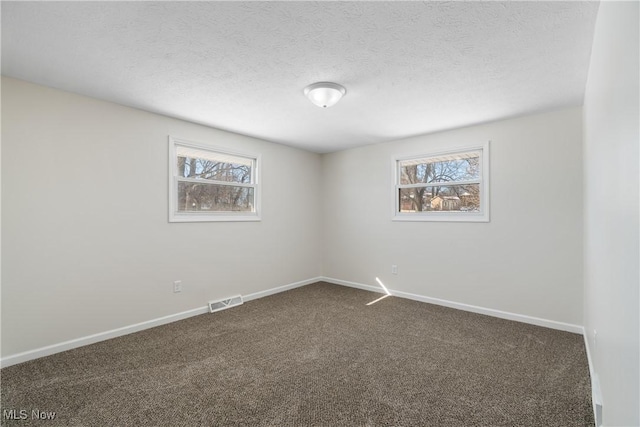 spare room with dark carpet, a textured ceiling, and a healthy amount of sunlight