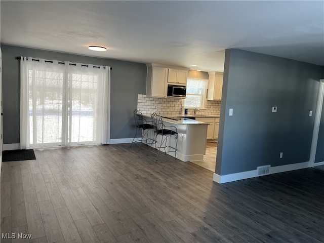 kitchen with sink, a breakfast bar area, white cabinetry, tasteful backsplash, and dark hardwood / wood-style flooring