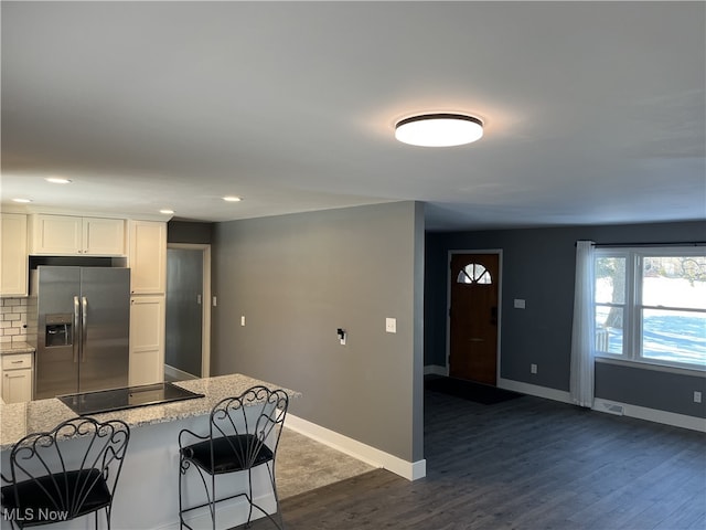 kitchen featuring a breakfast bar area, tasteful backsplash, stainless steel fridge with ice dispenser, black electric cooktop, and white cabinets