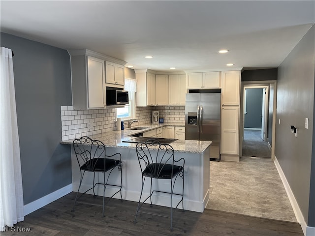 kitchen with wood-type flooring, kitchen peninsula, white cabinets, and appliances with stainless steel finishes