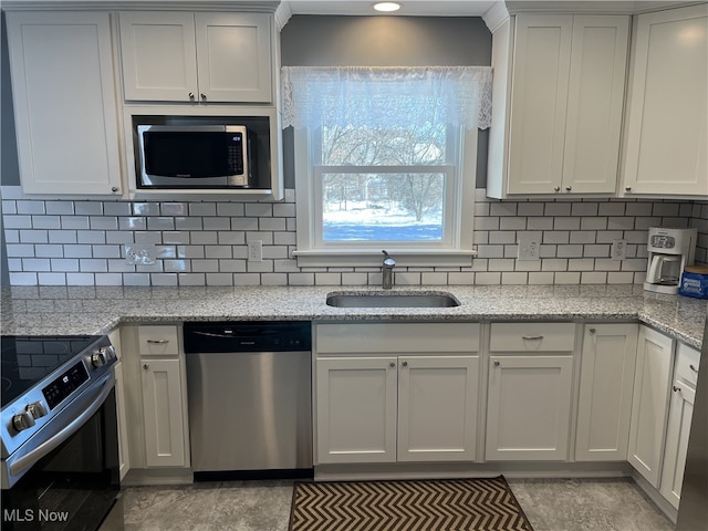 kitchen featuring stainless steel appliances, white cabinetry, sink, and light stone counters