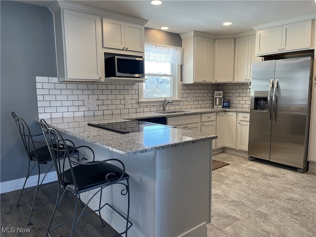 kitchen featuring sink, white cabinetry, kitchen peninsula, stainless steel appliances, and light stone countertops