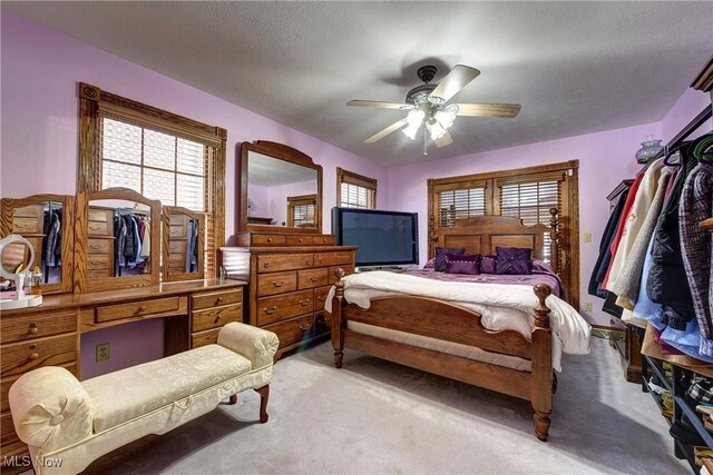 bedroom with ceiling fan, light colored carpet, and a textured ceiling