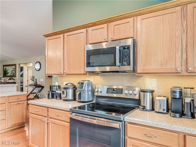 kitchen with light brown cabinetry, decorative backsplash, light hardwood / wood-style flooring, and stainless steel appliances