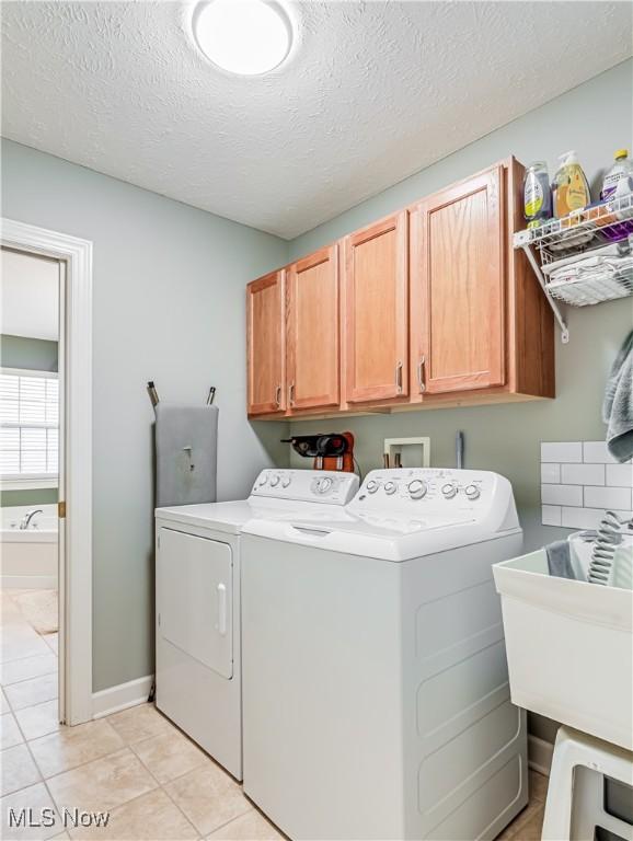 washroom with light tile patterned flooring, sink, cabinets, washer and dryer, and a textured ceiling