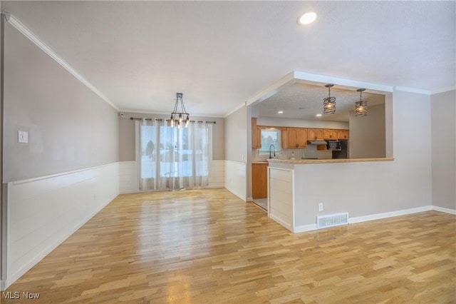 interior space with an inviting chandelier, ornamental molding, sink, and light hardwood / wood-style flooring