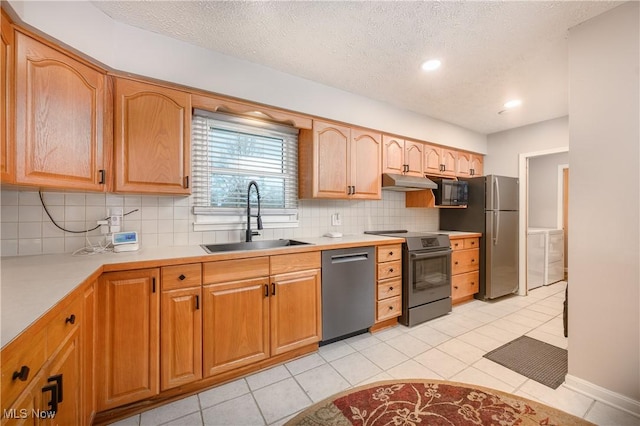 kitchen with sink, light tile patterned floors, washer and dryer, and appliances with stainless steel finishes