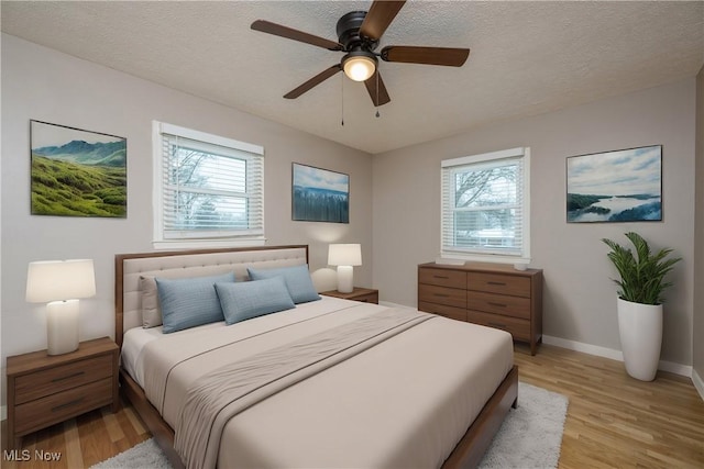 bedroom featuring ceiling fan, a textured ceiling, multiple windows, and light wood-type flooring