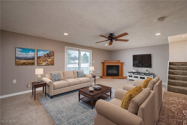 carpeted living room featuring ceiling fan, wooden walls, and a textured ceiling