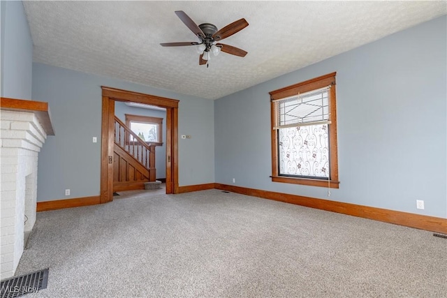 unfurnished living room featuring ceiling fan, plenty of natural light, carpet flooring, and a textured ceiling