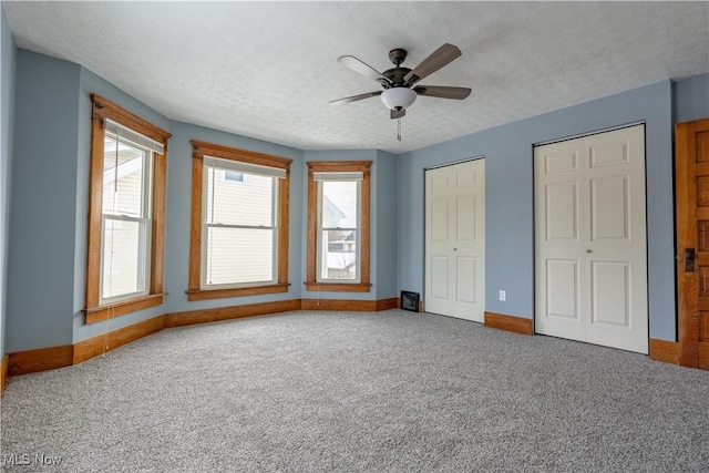 unfurnished bedroom with ceiling fan, carpet flooring, a textured ceiling, and two closets