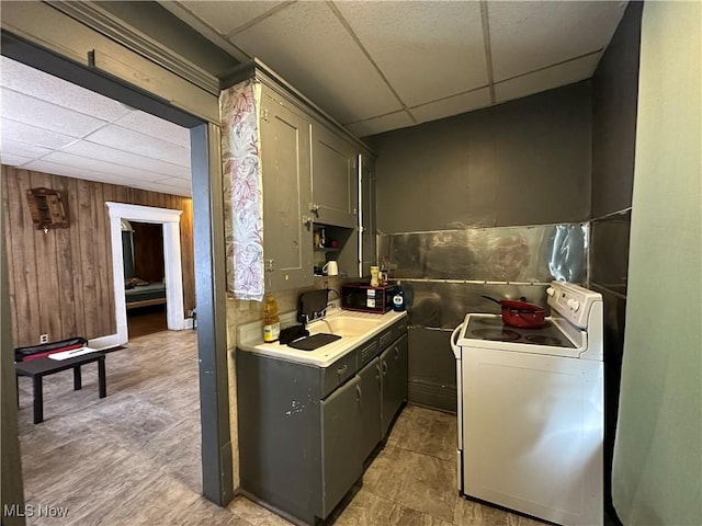 kitchen featuring white range with electric stovetop, wood walls, sink, gray cabinetry, and a drop ceiling