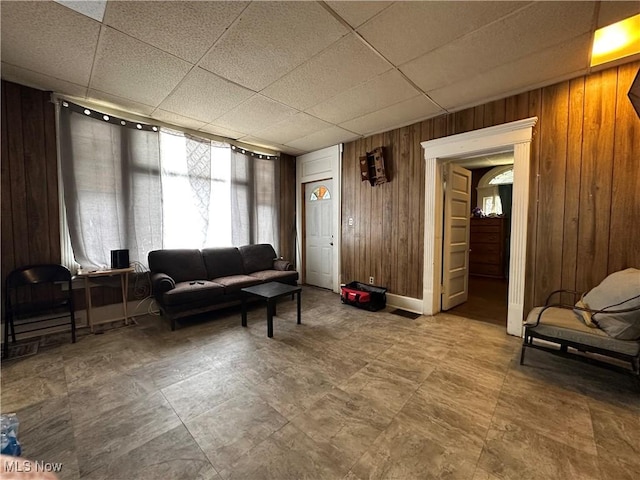 living room featuring a drop ceiling and wooden walls