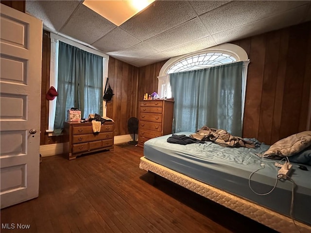 bedroom with wooden walls, a drop ceiling, and dark hardwood / wood-style flooring