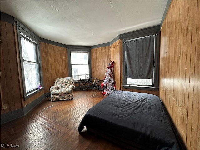 bedroom featuring multiple windows, dark wood-type flooring, and wooden walls