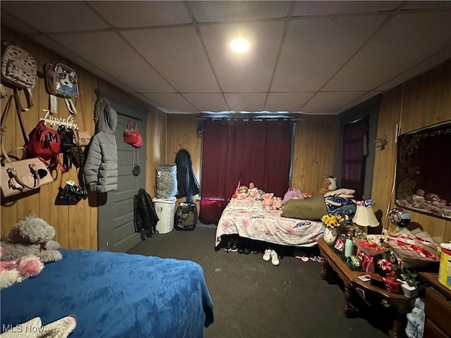 carpeted bedroom featuring a paneled ceiling and wooden walls