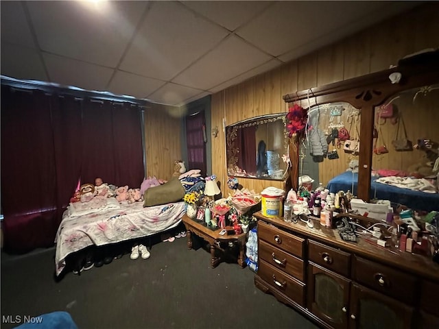 bedroom featuring a paneled ceiling and wood walls