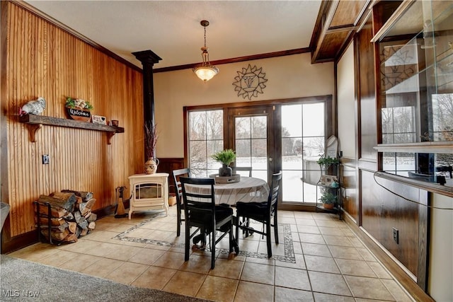 dining area featuring crown molding, wooden walls, light tile patterned flooring, and a wood stove