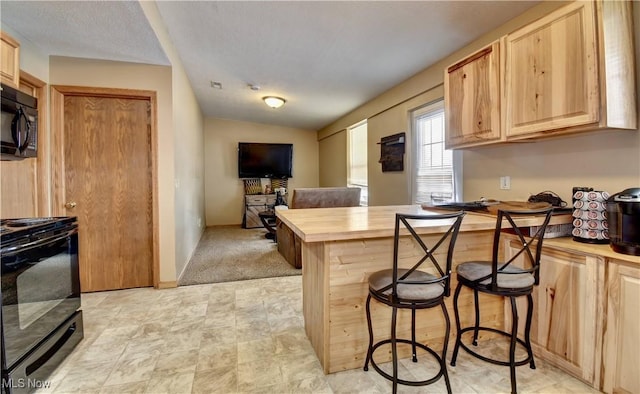 kitchen featuring wooden counters, light brown cabinetry, a breakfast bar area, and black appliances