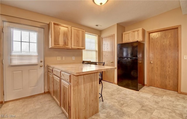 kitchen featuring black fridge, a breakfast bar area, light brown cabinets, and kitchen peninsula