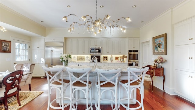 kitchen featuring dark wood-type flooring, decorative light fixtures, a center island with sink, stainless steel appliances, and light stone countertops