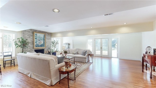 living room with a brick fireplace, plenty of natural light, light hardwood / wood-style floors, and french doors