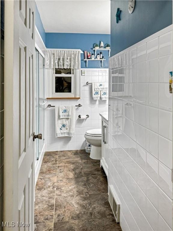 bathroom featuring vanity, a shower with shower door, tile walls, and toilet