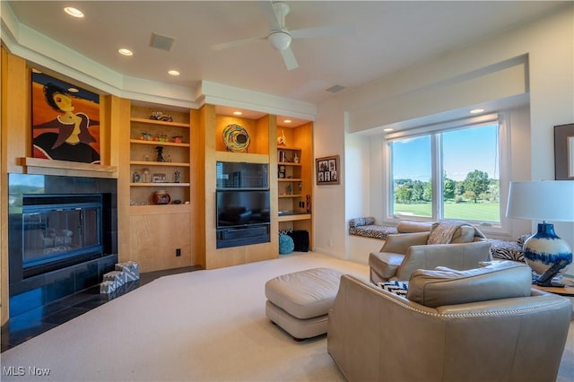 living room featuring a tiled fireplace, built in shelves, and ceiling fan