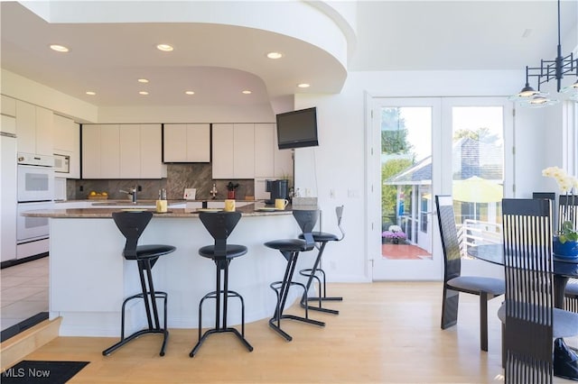 kitchen with a kitchen breakfast bar, tasteful backsplash, white appliances, and decorative light fixtures